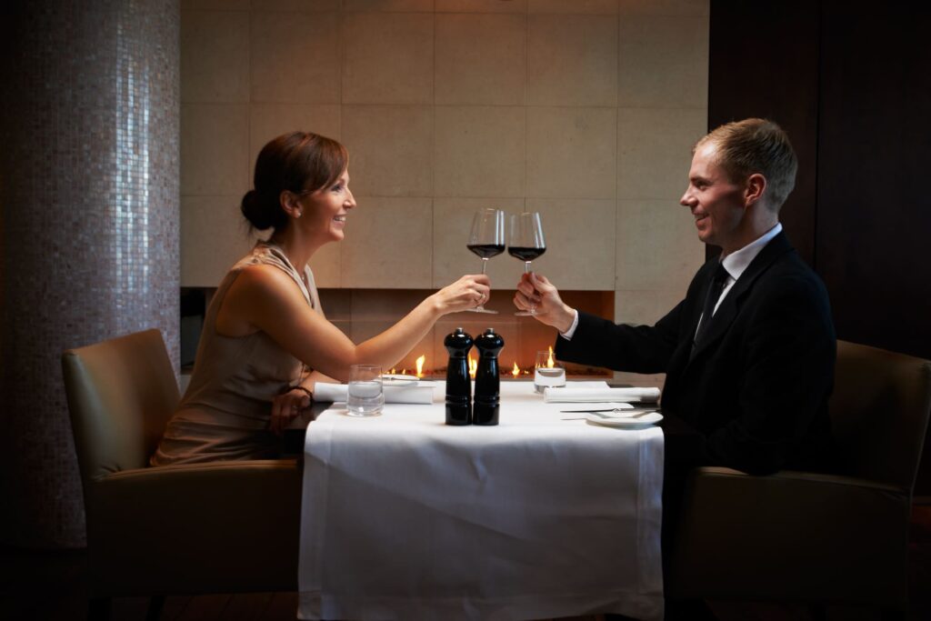 Ein Geschäftsmann und eine elegante Dame genießen ein romantisches Abendessen bei Kerzenschein in einem gehobenen Restaurant in Frankfurt, symbolisch für erstklassige Begleitung und exzellente Gastlichkeit.