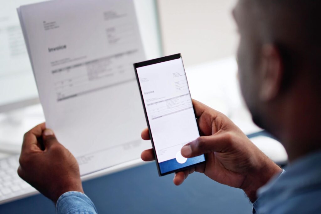 Mann scannt ein Dokument mit seinem Smartphone, um die Effizienz durch Fotos digitalisieren lassen und die Digitalisierung von Geschäftsunterlagen zu steigern.