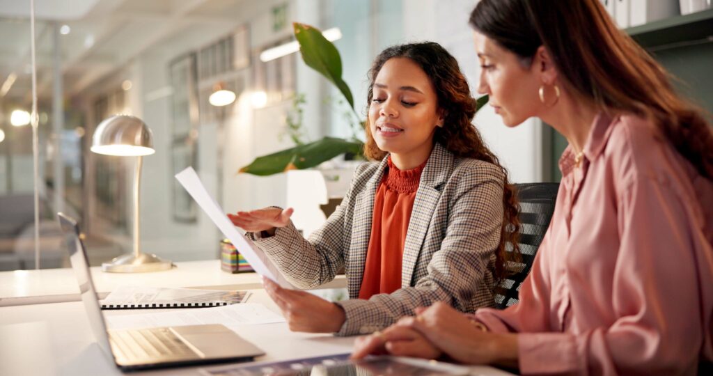 Zwei Geschäftsfrauen analysieren ein Dokument im Büro. DocuWare Software unterstützt digitale Workflows und optimiert Teamarbeit.