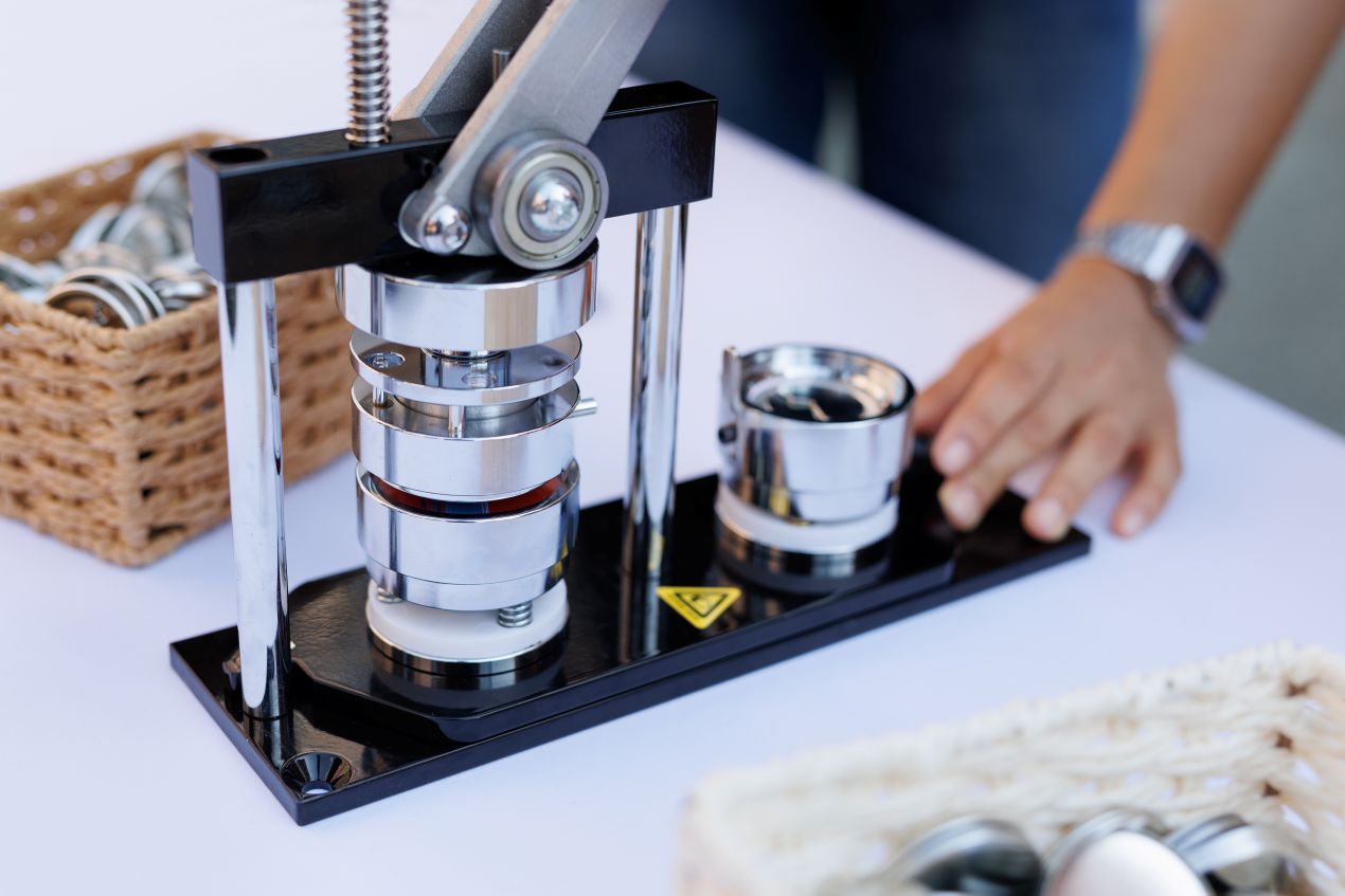 Eine manuelle Buttonmaschine auf einem Tisch mit Zubehör – Buttonproduktion bei Event oder Messe