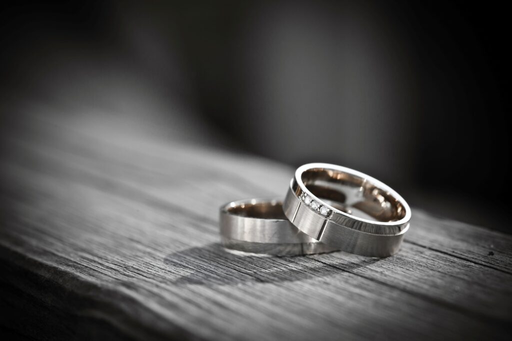 Zwei moderne Eheringe aus Silber auf Holz, einer mit Diamantbesatz